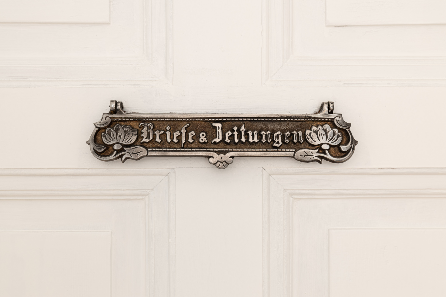 Historischer Briefschlitz mit der Aufschrift ‚Briefe & Zeitungen‘ in einer Altbauwohnung, der nostalgische Akzente setzt.