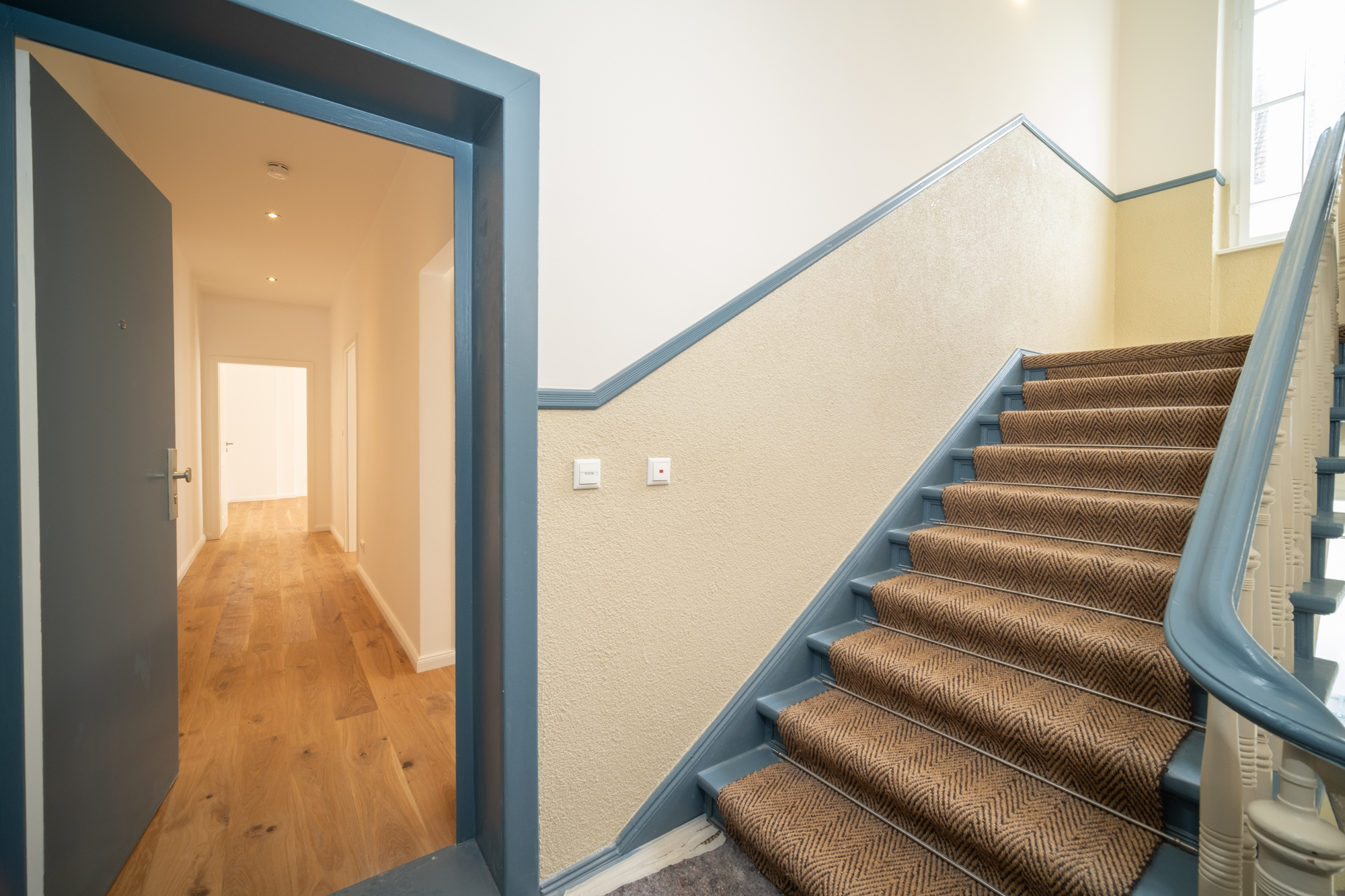 Renovated staircase of an old building with blue-painted banisters and modern wooden floor, showing the transition from historical architecture to modernized living comfort.